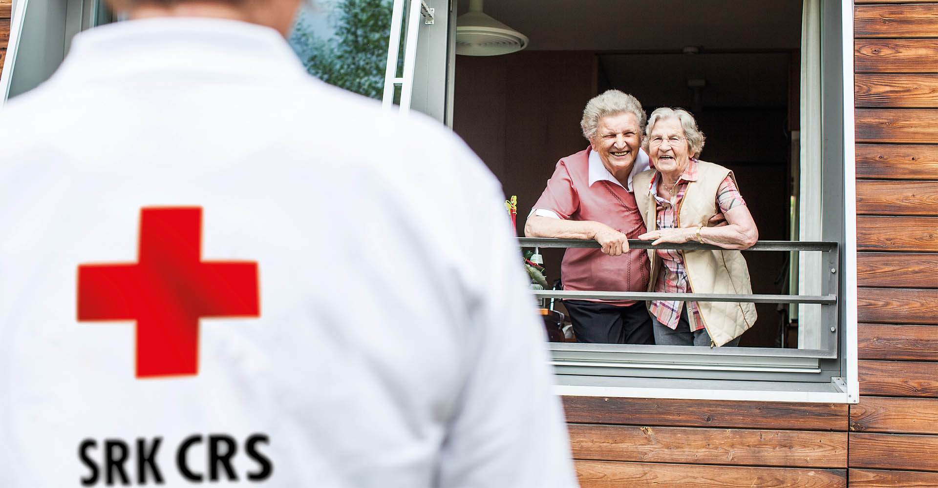 Ein Mitarbeiter des Roten Kreuzes begrüßt zwei ältere Damen (Foto)